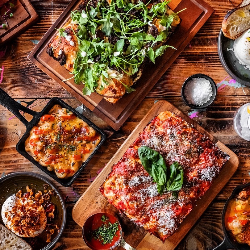 A spread of food from POP Kitchen including macaroni cheese and Detroit style pizza topped with basil leaves and rocket salad
